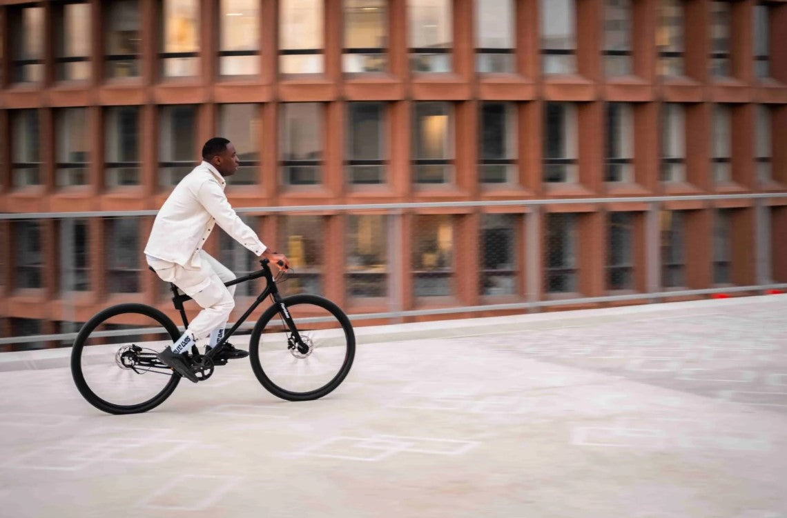 Action shot of a man riding a black Ref Essential bike, blurred background emphasizing speed and city life.