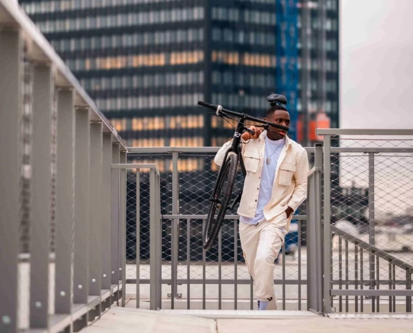 Fashionable urban commuter carrying a black Ref Essential bike upstairs, merging active lifestyle with city vibes.