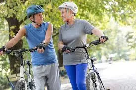 Two elderly walking their folding bikes in the park