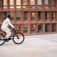 Action shot of a man riding a black Ref Essential bike, blurred background emphasizing speed and city life.
