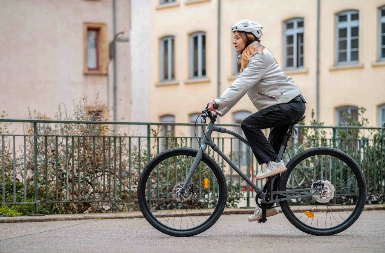 Woman riding Essential Boost bike in urban setting, showcasing its practical design for city commuting.