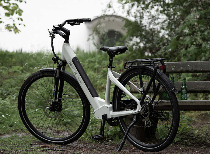 Deruiz Quartz electric bicycle parked by a wooden bench in a natrual outdoor setting.