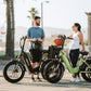 A couple enjoying a conversation next to their Eskute Star eBikes on a sunny boardwalk.